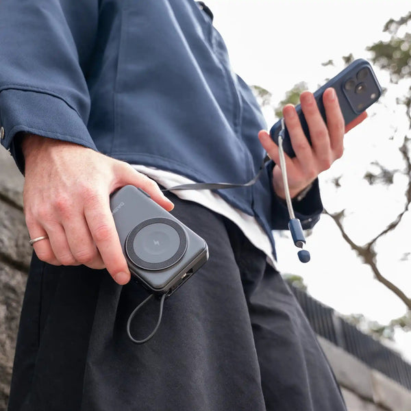Person holding a phone, and a power bank outdoors.