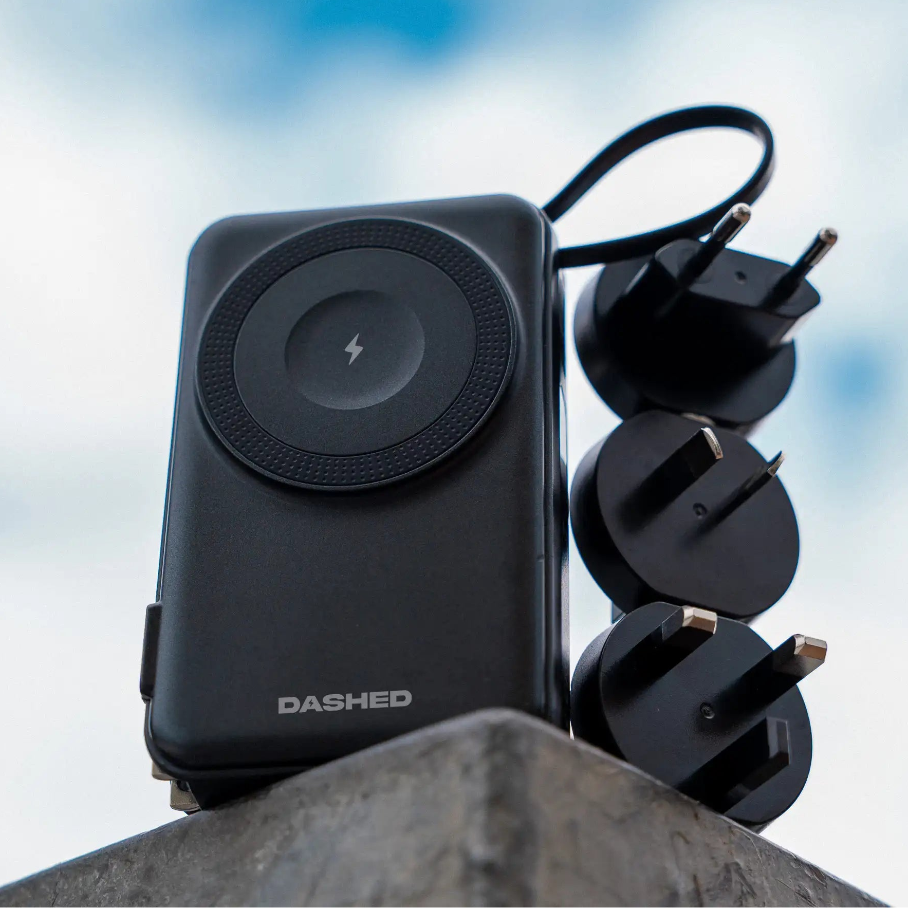 Black charging device with multiple outlets against a blue sky background